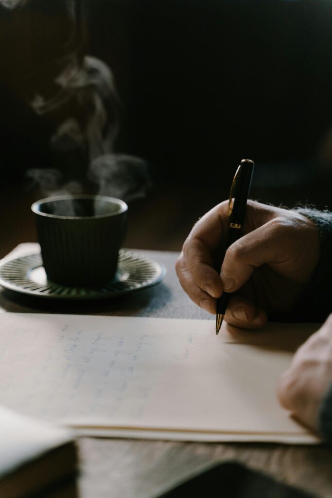 A person writing a heartfelt letter with a pen beside a warm cup — symbolizing the courage to raise your voice through words.