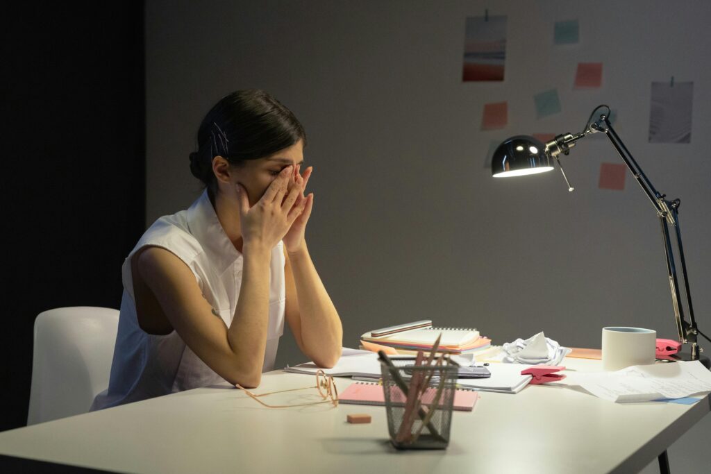 Overwhelmed teacher sitting at desk, covering face in stress — representing the emotional toll of the Indian education system on educators.”