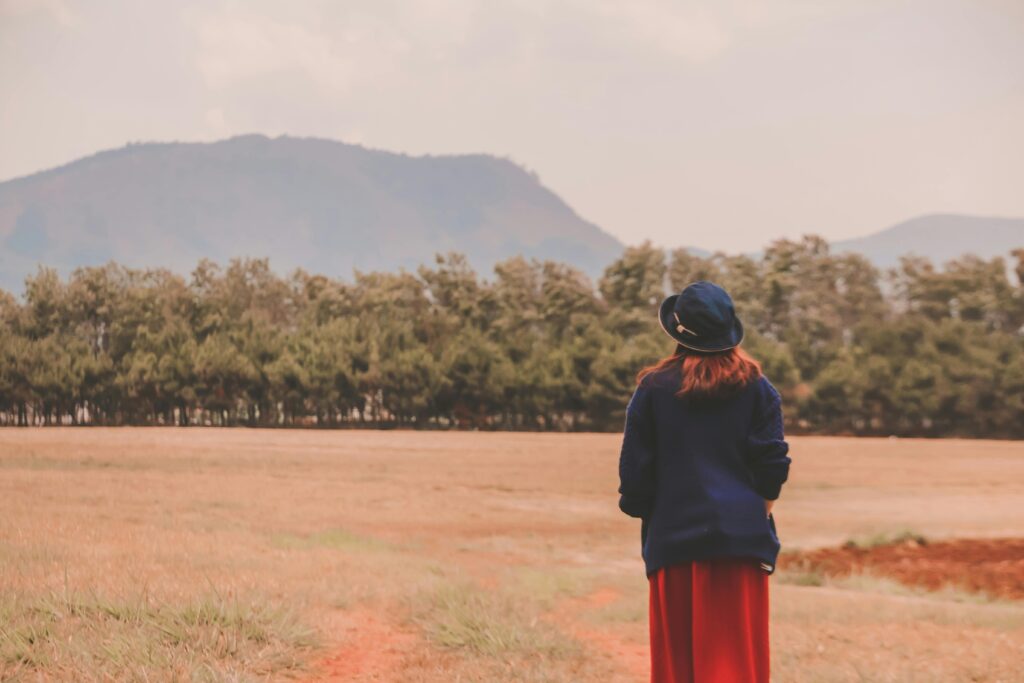 A girl standing alone in an open field, facing the mountains — symbolizing inner strength to raise your voice even when no one listens.