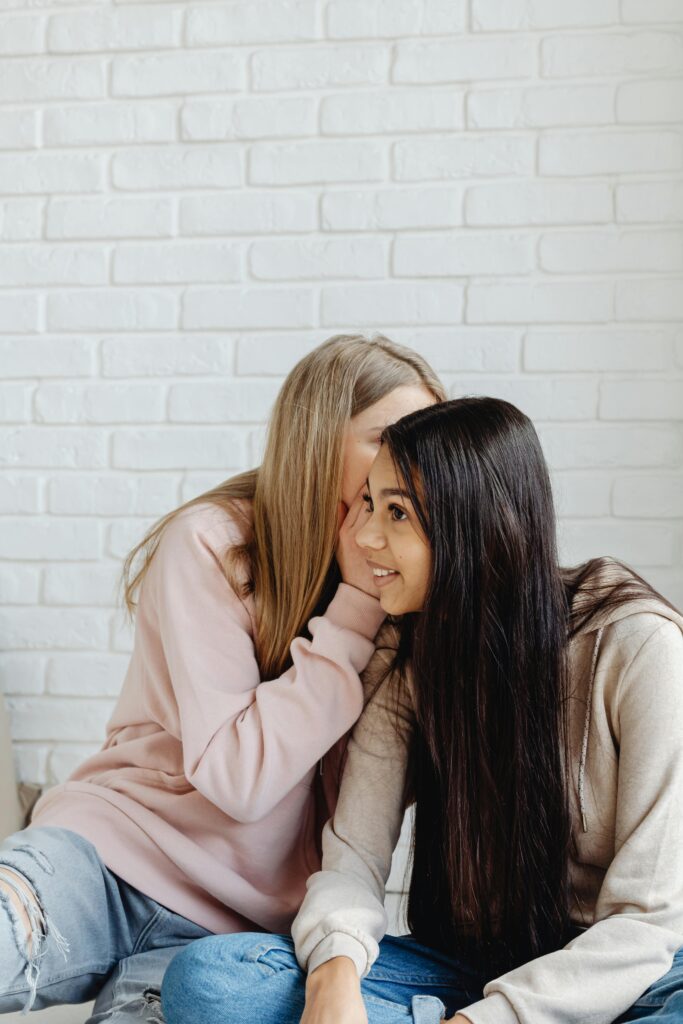 Two friends whispering secretly, representing gossiping and its hidden effects.